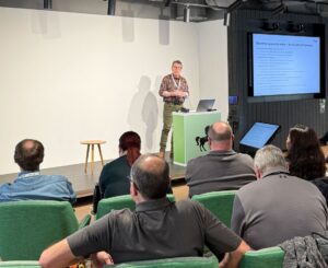 Gareth Copplestone-Jones standing in front of an audience, presenting powerpoint slides on a big screen.